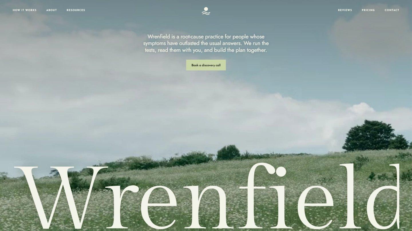 The Wrenfield home page: a small uppercase nav and the mark over a wildflower meadow under a cloudy sky, a tagline and a sage button in the sky, and the practice’s name in a large serif spanning the width along the bottom of the photo.